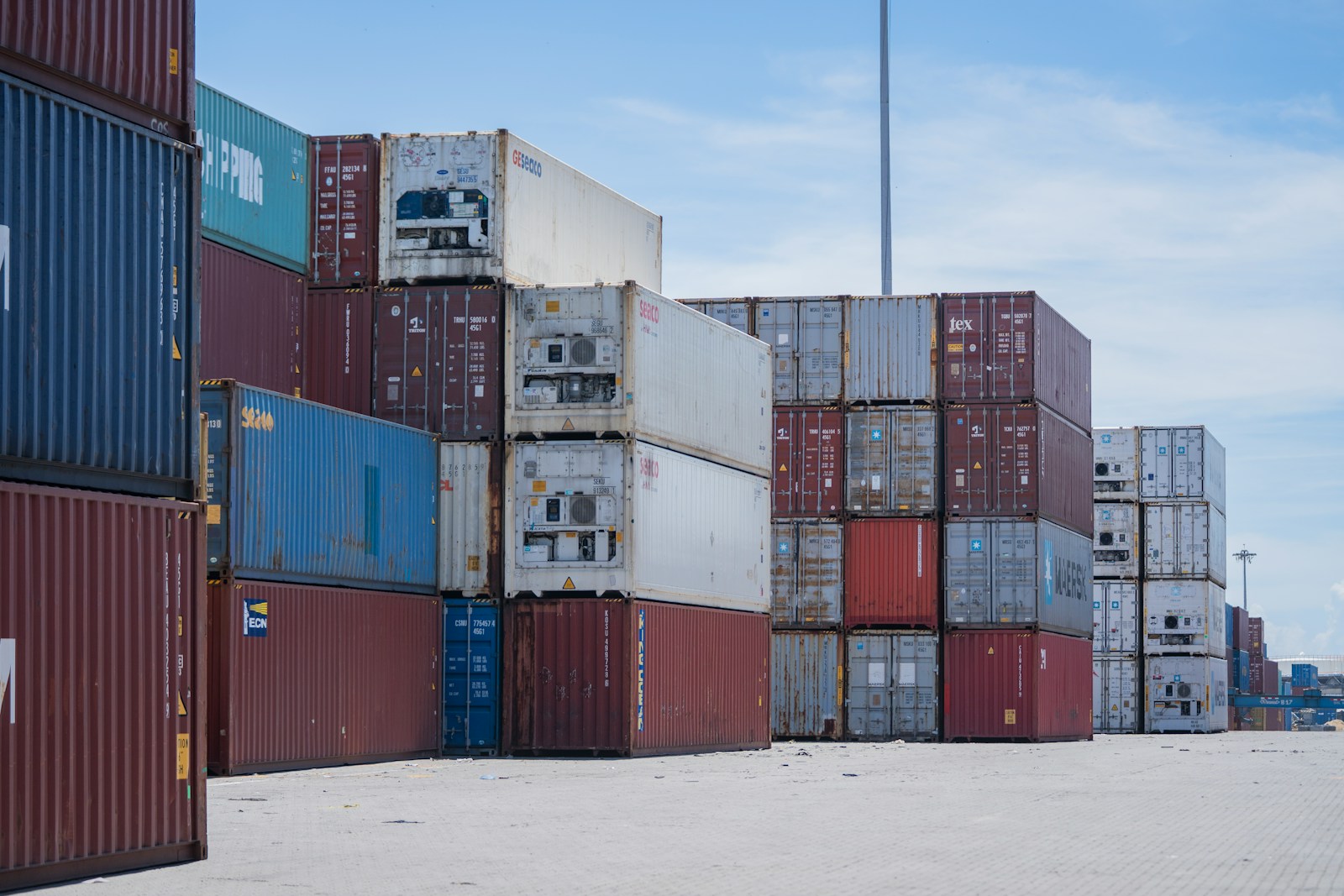 Stacked shipping containers at a port under a blue sky